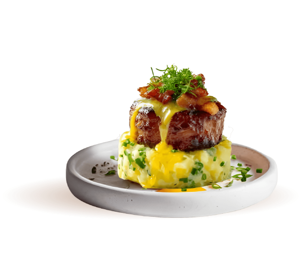 A gourmet plated entrée featuring a thick, seared beef filet steak stacked on top of a bed of herb-flecked mashed potatoes, drizzled with a rich yellow sauce and topped with crispy bacon bits and fresh microgreens.